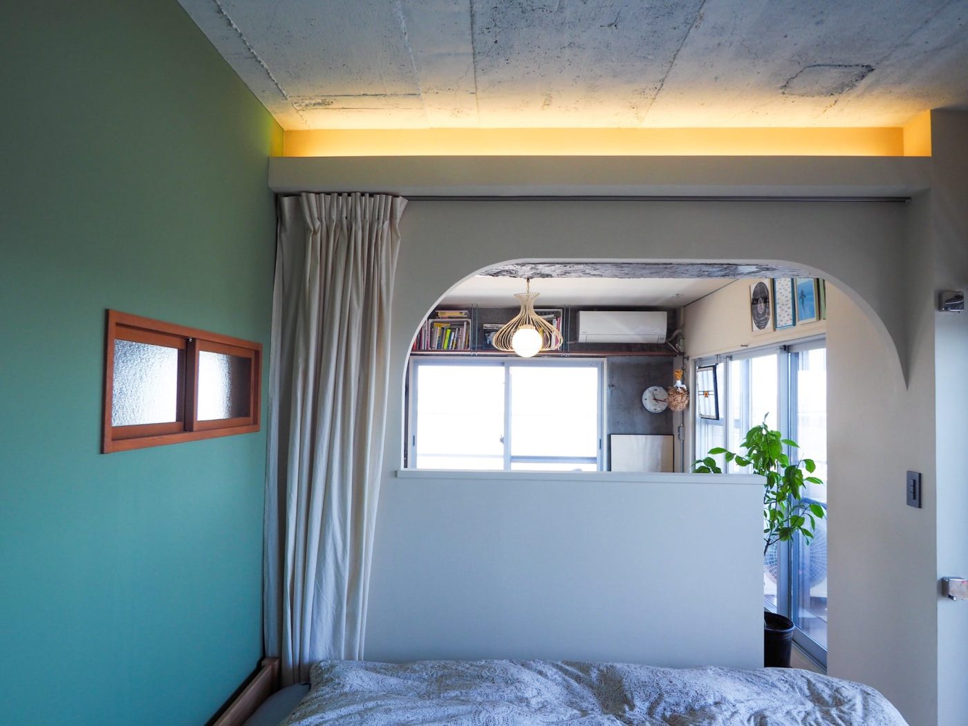 グリーンの壁が可愛らしい寝室。アーチの先がリビングです。ニンニク型の照明がアイコニック。